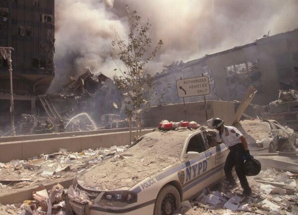 پس از حمله تروریستی 11 سپتامبر به مرکز تجارت جهانی، در حالی که آتش نشانان شهر نیویورک روی خرابه های در حال دود شدن در پس زمینه آب می پاشند یک امدادگر به موتر پولیس نزدیک می شود. - اسپوتنیک افغانستان  