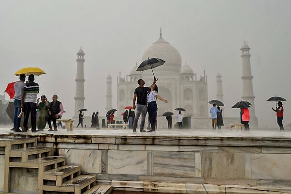 گردشگران هنگام بازدید از تاج محل در هند هنگام بارش باران در آگرا در 9 اکتبر 2022، چتر در دست دارند و عکس می گیرند. - اسپوتنیک افغانستان  