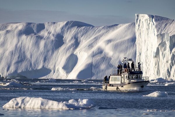 یک قایق حامل گردشگران در 30 جون 2022 در میان کوه‌های یخی شناور در خلیج دیسکو، ایلولیسات، گرینلند غربی، حرکت می کند. - اسپوتنیک افغانستان  