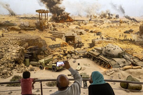 مردم در هنگام بازدید از موزه &quot;نمای پانورامای جنگ 6 اکتبر&quot; و یادبود جنگ اعراب و اسرائیل در سال 1973 در قاهره در یک نمایش از صحنه جنگ بازآفرینی شده. - اسپوتنیک افغانستان  
