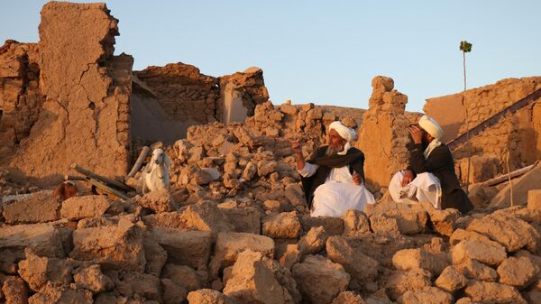 Люди сидят у развалин дома после землетрясения в деревне Сарбуланд Зенде Джана, район провинции Герат, Афганистан - اسپوتنیک افغانستان  