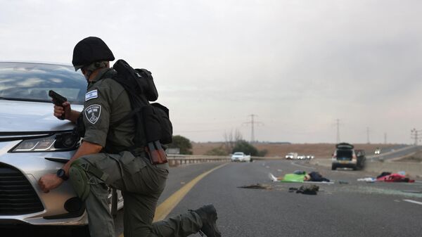 An Israeli soldiers take cover behind a car as he looks toward bodies on a main road near the Gevim Kibbutz, close to the border with Gaza on October 7, 2023. - اسپوتنیک افغانستان  