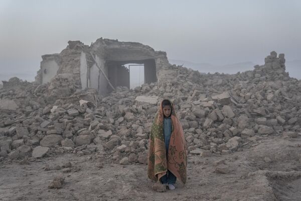 یک پسر افغان در مقابل خانه‌اش که در اثر زلزله در ولسوالی زنده جان ولایت هرات ویران شده ایستاده است. - اسپوتنیک افغانستان  