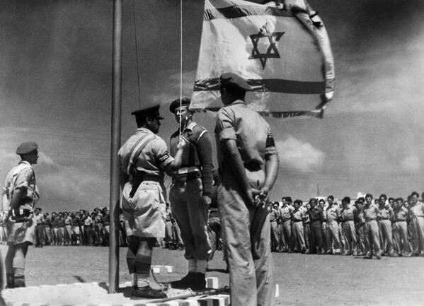 تصویری که در 8 جون 1948 منتشر شد، یک افسر اسرائیلی را نشان می دهد که پرچم ملی را برای اولین بار در جشن پیدایش دولت اسرائیل پس از اعلام آن، در 14 می 1948 برافراشته است. - اسپوتنیک افغانستان  