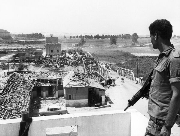 یک سرباز اسرائیلی در 22 جون 1967 پناهندگان فلسطینی را در حال عبور از پل جنگ زده آلنبی برای رسیدن به ساحل  شرقی اردن، تماشا می کند. - اسپوتنیک افغانستان  