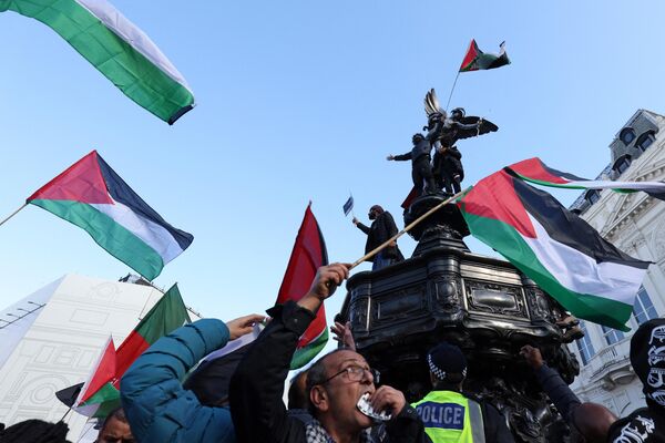 معترضان که پرچم فلسطین را در دست دارند، در حین تظاهرات ملی طرفدار فلسطین در لندن، بر مجسمه ی اروس در پیکادیلی سیرک صعود می کنند. - اسپوتنیک افغانستان  