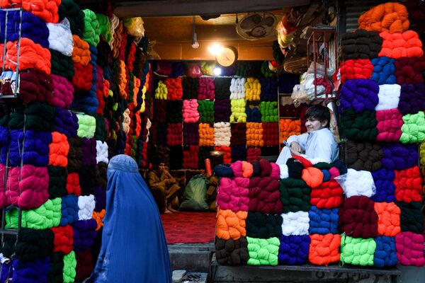 یک زن افغان چادری پوش در یکی از بازار مازاری شریف از کنار مغازه نخ فروشی عبور می کند. - اسپوتنیک افغانستان  
