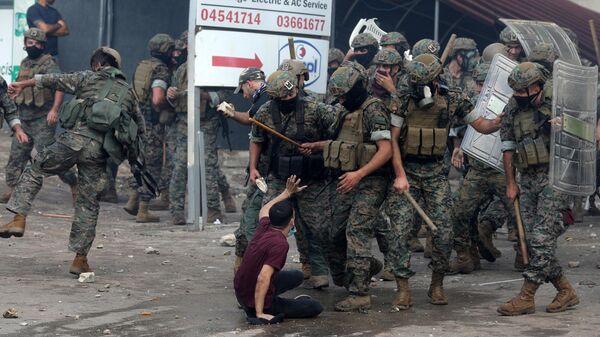 Силы безопасности Ливана угрожают молодому человеку дубинками во время столкновения с протестующими возле посольства США в Аукаре к востоку от Бейрута - اسپوتنیک افغانستان  
