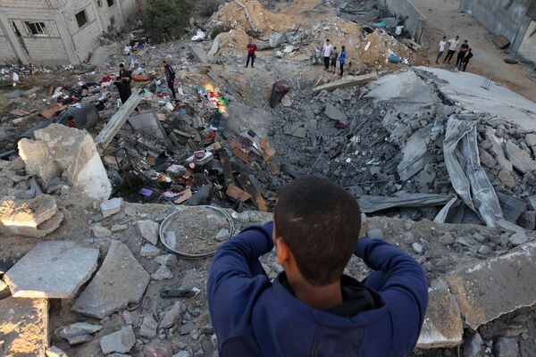 مردی در حالی که مردم ساختمان های ویران شده در بمباران اسرائیل در رفح در جنوب نوار غزه سرگردان هستند، نگاه می کند. - اسپوتنیک افغانستان  