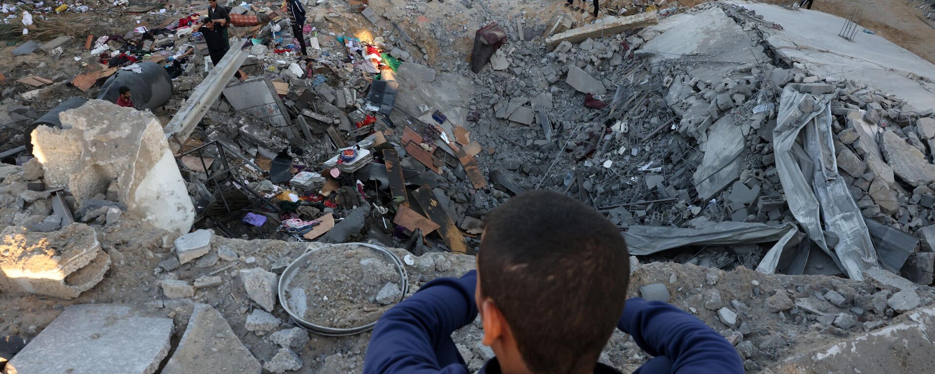 Мальчик наблюдает, как люди разбирают обломки здания, разрушенного в результате израильской бомбардировки в Рафахе на юге сектора Газа - اسپوتنیک افغانستان  , 1920, 24.10.2023