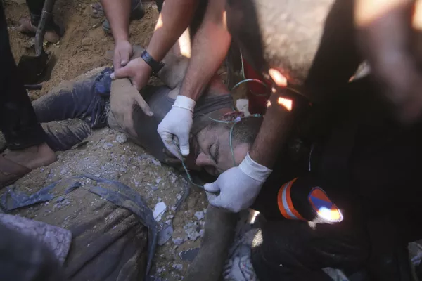 فلسطینی ها یک مرد مجروح را از زیر آوار ساختمان ویران شده در پی حمله هوایی اسرائیل به رفح در نوار غزه نجات دادند. - اسپوتنیک افغانستان  