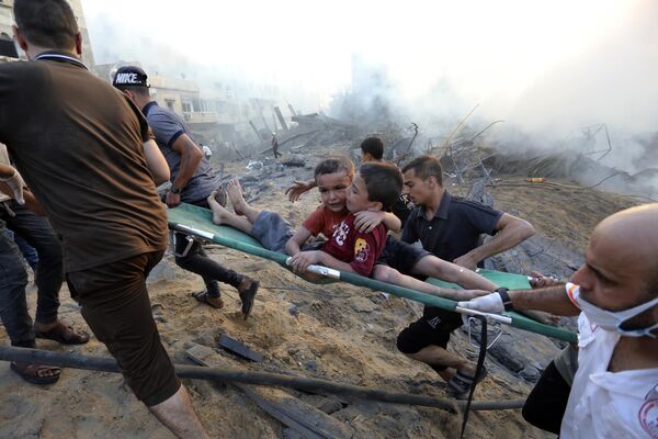 فلسطينی ها دو پسر زخمی را از زير خانه های ويران شده در اثر حمله هوايی اسرائيلی به غزه خارج می کنند - اسپوتنیک افغانستان  