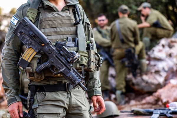 یک سرباز ارتش اسرائیل در 28 اکتبر 2023 با یک تفنگ تهاجمی که روی سینه‌ حمل می کند در موقعیتی در منطقه جلیل بالایی در شمال اسرائیل در نزدیکی مرز با لبنان ایستاده است. - اسپوتنیک افغانستان  