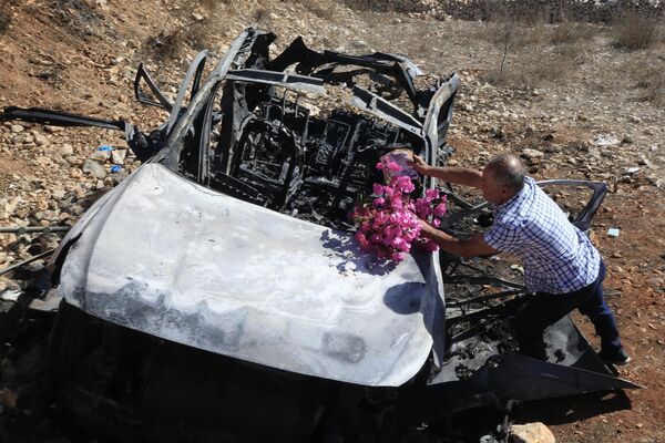 یک مرد لبنانی روی لاشه موتری که در آن بستگانش در جریان حمله اسرائیل در جنوب لبنان در نزدیکی مرز با اسرائیل کشته شدند، گل می‌گذارد. - اسپوتنیک افغانستان  