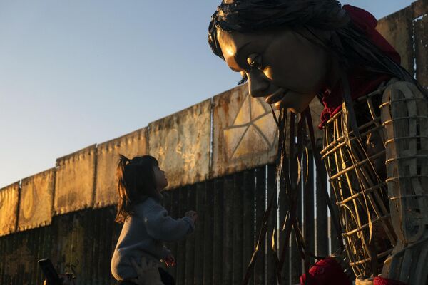 کودکی به امل کوچک، عروسکی 12 فوتی که نماینده یک کودک پناهجوی سوری ده ساله است، در نزدیکی دیوار مرزی ایالات متحده و مکسیکو در پلیاس د تیجوانا، ایالت باخا کالیفرنیا، خوش آمد می گوید. - اسپوتنیک افغانستان  