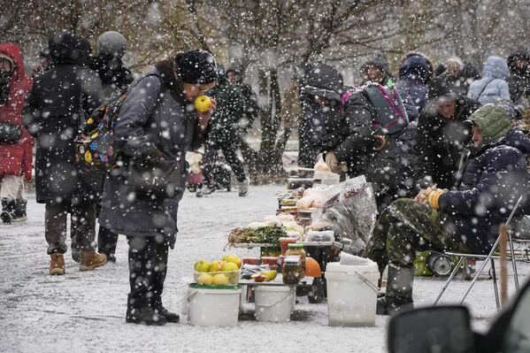 زنی در جریان بارش برف در سن پترزبورگ از یک فروشنده خیابانی سیب می چیند و می خرد. - اسپوتنیک افغانستان  