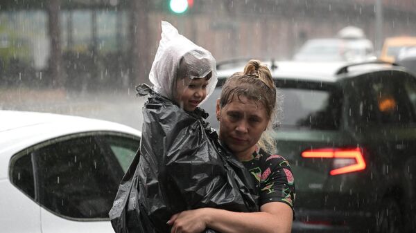 Женщина с ребенком на улице Москвы во время сильного ливня - اسپوتنیک افغانستان  