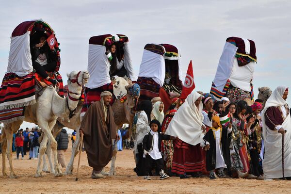 مجریانی که لباس‌های سنتی بر تن دارند، در جریان نمایشی در آغاز پنجاه و پنجمین جشنواره بین‌المللی صحرا در دوز، در جنوب تونس، شتر سواری می‌کنند. 27 دسامبر 2023 - اسپوتنیک افغانستان  