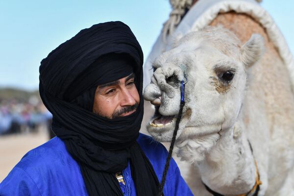 مجری با لباس سنتی در حین نمایش در آغاز جشنواره بین المللی صحرا در دوز، در جنوب تونس، کنار شتر ایستاده است. 27 دسامبر 2023 - اسپوتنیک افغانستان  