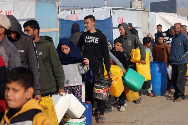 فلسطینی‌های آواره برای تامین آب خود از کامیونی که توسط سازمان غیردولتی پزشکان بدون مرز در یک کمپ چادری موقت در رفح در نزدیکی مرز با مصر در جنوب نوار غزه سازماندهی شده است، صف ‌کشیده اند. - اسپوتنیک افغانستان  