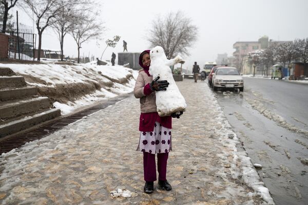  دختر افغان در 19 فبروری 2024 یک آدم برفی را در امتداد سنگفرش پر از برف در کابل حمل می کند. (عکس از وکیل کوهسار / خبرگزاری فرانسه) - اسپوتنیک افغانستان  