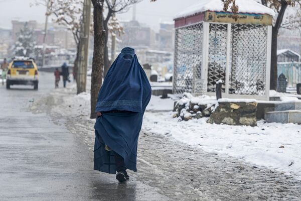 یک زن برقع پوش افغان در 19 فوریه 2024 از کنار خیابانی در امتداد گورستان پر از برف در کابل عبور می کند. (عکس از وکیل کوهسار / خبرگزاری فرانسه) - اسپوتنیک افغانستان  