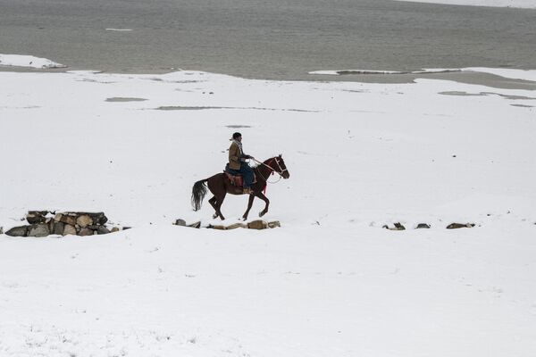 مرد افغان در 19 فبروری 2024 سوار بر اسب از دریاچه پر برف قرغه در حومه کابل در 19 فوریه 2024 عبور می کند. (عکس از وکیل کوهسار / خبرگزاری فرانسه) - اسپوتنیک افغانستان  