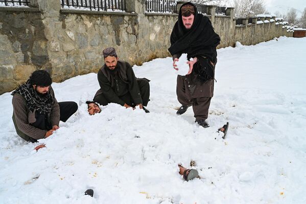 سه جوان افغان  که یکی را در برف دفن کرده اند، در پی بارش برف در ولسوالی پغمان در حومه کابل در 19 فبروری 2024 قدرت خود را آزمایش می کند. (عکس از وکیل کوهسار / خبرگزاری فرانسه) - اسپوتنیک افغانستان  