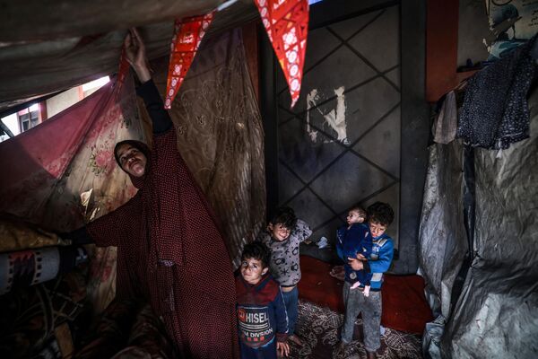 یک زن آواره فلسطینی به همراه کودکان در بحبوحه نبردهای جاری بین اسرائیل و گروه شبه نظامی حماس در چادر خود در اردوگاهی در کنار خیابانی در رفح در 14 مارچ 2024. درگیری اسرائیل و حماس که از 7 اکتوبر آغاز شده است، منجر به تلفات انبوه غیرنظامیان شده، مناطق وسیعی را به یک زمین بایر پر از آوار تبدیل کرده و هشدارهایی را درباره گرسنگی زودهنگام در این سرزمین فلسطینی با 2.4 میلیون نفر جمعیت به دنبال داشته است. - اسپوتنیک افغانستان  