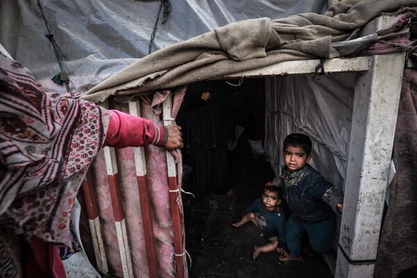 کودکان آواره فلسطینی در 14 مارچ 2024، در میان نبردهای جاری بین اسرائیل و گروه شبه نظامی حماس، در اردوگاهی در کنار خیابانی در شهر رفح عکس می گیرند. درگیری اسرائیل و حماس که از 7 اکتوبر آغاز شده است، منجر به تلفات انبوه غیرنظامیان شده، مناطق وسیعی را به یک زمین بایر پر از آوار تبدیل کرده و هشدارهایی را درباره گرسنگی زودهنگام در این سرزمین فلسطینی با جمعیت  2.4 میلیون نفر به دنبال داشته است. - اسپوتنیک افغانستان  