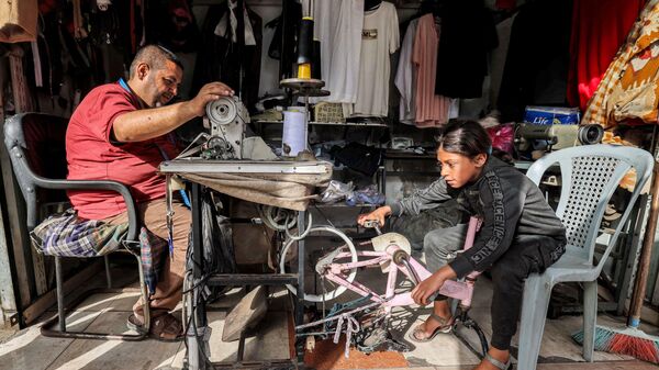Девочка крутит педали велосипеда, превращенного в импровизированный источник энергии для портного, работающего на швейной машине, Рафах - اسپوتنیک افغانستان  
