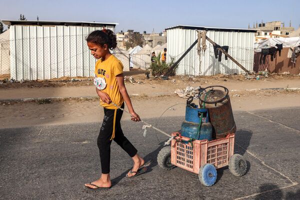 یک دختر در 23 اپریل 2024 در بحبوحه درگیری های جاری در خاک فلسطین بین اسرائیل و گروه شبه نظامی حماس، گاری پر از سیلندرهای گاز را در امتداد جاده در رفح در جنوب نوار غزه می کشد. (عکس از MOHAMMED ABED / AFP) - اسپوتنیک افغانستان  