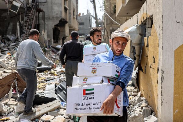 مردان با بسته‌های کمک‌های بشردوستانه که در 23 اپریل 2024 در بحبوحه درگیری‌های جاری در خاک فلسطین بین اسرائیل و گروه شبه‌نظامی حماس جمع‌آوری شده بود، از ساختمان‌های آسیب‌دیده عبور می‌کنند. (عکس از خبرگزاری فرانسه) - اسپوتنیک افغانستان  