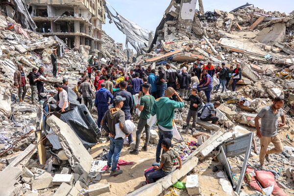 مردم در 23 اپریل 2024 در کنار یک ساختمان ویران شده در محل پرتاب کمک های بشردوستانه در شمال نوار غزه در بحبوحه درگیری های جاری در خاک فلسطین بین اسرائیل و گروه شبه نظامی حماس جمع می شوند. (عکس از خبرگزاری فرانسه) - اسپوتنیک افغانستان  