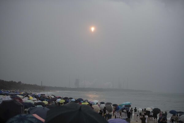 جمعیتی از ساحل تماشا می‌کنند که راکت لانگ مارس 5، حامل کاوشگر مهتاب ماموریت چانگ ای-6، با بارش باران در مرکز پرتاب فضایی Wenchang در استان هاینان در جنوب چین در 3 می 2024 بلند می‌شود. - اسپوتنیک افغانستان  