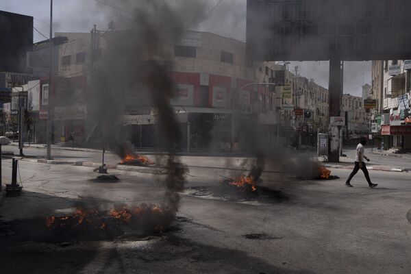 مردی فلسطینی در جریان درگیری با نیروهای اسرائیلی در شهر جنین در کرانه باختری، چهارشنبه 22 می 2024 از کنار لاستیک های سوخته عبور می کند. - اسپوتنیک افغانستان  