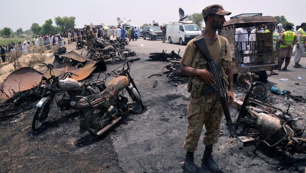 A soldier stands guard amid burnt out cars and motorcycles at the scene of an oil tanker explosion in Bahawalpur, Pakistan - اسپوتنیک افغانستان  
