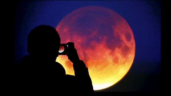 A man takes picture of the screen displaying the moon, appearing in a dim red colour, which is covered by the Earth's shadow during a total lunar eclipse in Warsaw, Poland September 28, 2015 - اسپوتنیک افغانستان  