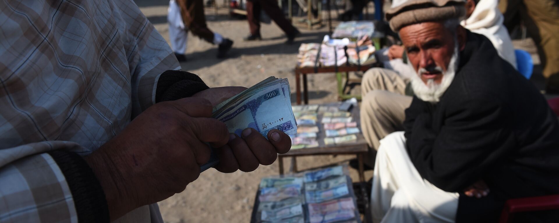 In this photograph taken on December 29, 2014, an Afghan customer (L) counts his Afghani currency notes at a currency exchange market along the roadside in Kabul - اسپوتنیک افغانستان  , 1920, 16.12.2021