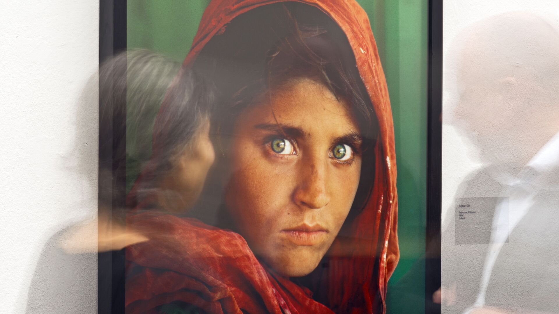 In this picture taken with a long time exposure people walk in front of the photo 'Afghan Girl' (Pakistan, 1984) during the exhibition 'Steve McCurry Retrospective' of US photographer Steve McCurry in the Kunsthalle (Art Hall) in Erfurt, Germany, Wednesday, Feb. 26, 2014.  - اسپوتنیک افغانستان  , 1920, 27.11.2021