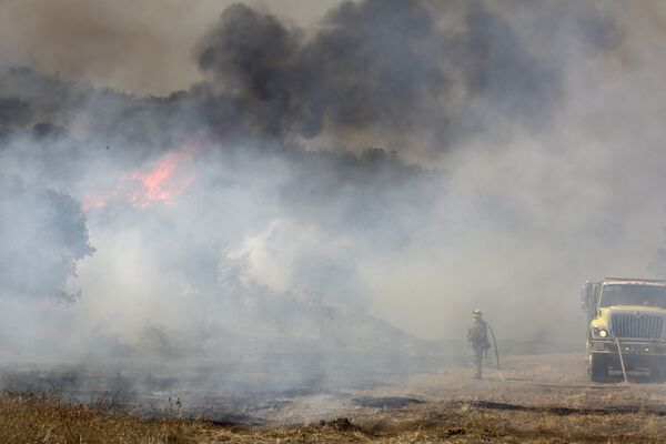 A firefighter is dwarfed by a burning mountain at the 6,500 acre Border Fire in eastern San Diego County, California, in the late afternoon on June 22, 2016. - اسپوتنیک افغانستان  