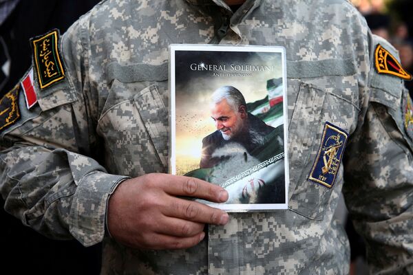 یک مرد نظامی‌پوش تصویر جنرال سلیمانی را در دست گرفته است - اسپوتنیک افغانستان  