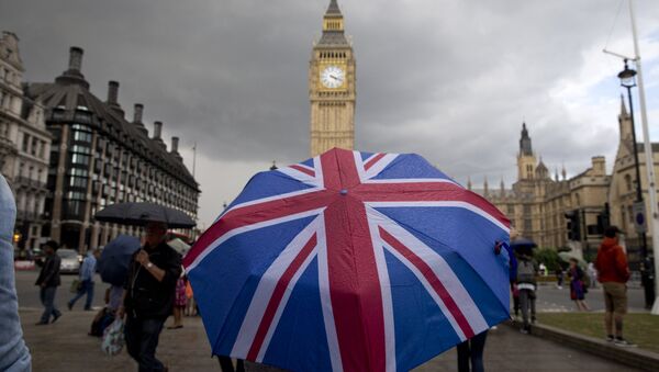 A pedestrian shelters from the rain beneath a Union flag themed umbrella as they walk near the Big Ben clock face and the Elizabeth Tower at the Houses of Parliament in central London on June 25, 2016 - اسپوتنیک افغانستان  