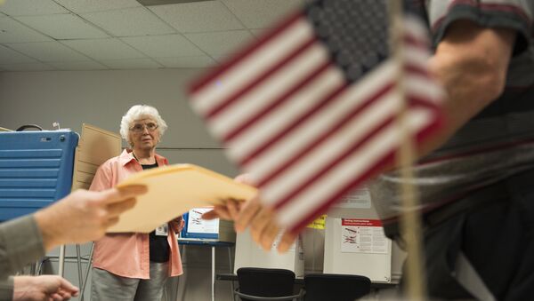 An election official watches as a man takes a ballot at an in-person absentee voting station in Fairfax, Virginia on October 12, 2016 - اسپوتنیک افغانستان  