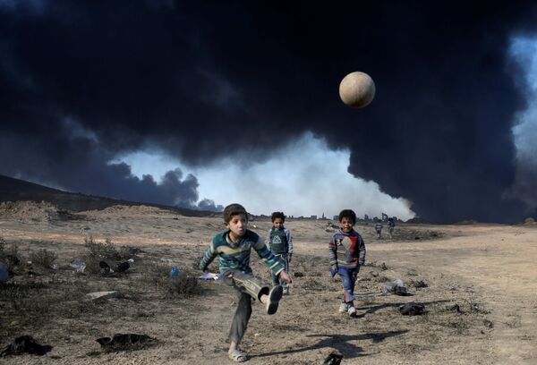 پسر ها به دنبال توپ درجنوب موصل در برابر چشم انداز دود از نفت شعله ور - اسپوتنیک افغانستان  